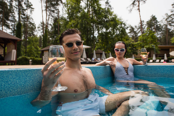 Man holding glass of wine near blurred girlfriend in pool  - Фото, зображення