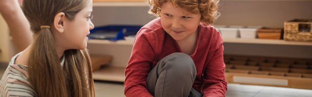 redhead boy smiling while looking at girl in montessori school, banner - Foto, Imagem