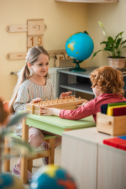 smiling girl playing game with wooden elements near curly boy, blurred foreground - Zdjęcie, obraz