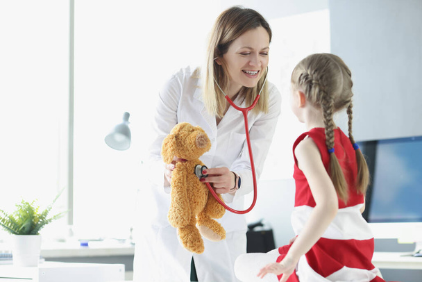 Pediatrician shows little girl how to use stethoscope using toy as example - Photo, Image