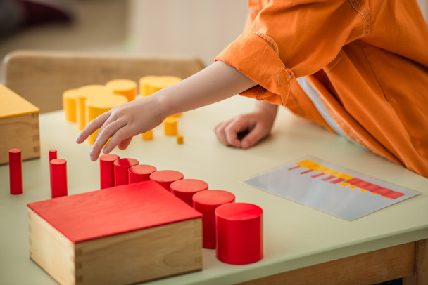 καλλιεργημένη άποψη του αγοριού παίζει με κόκκινο και κίτρινο κυλίνδρους στο Montessori σχολείο - Φωτογραφία, εικόνα