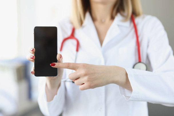 Doctor in white coat holds smartphone and points at it with hand closeup - Photo, Image