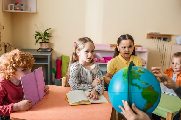 montessori school leraar tonen globe naar multiculturele kinderen tijdens de les - Foto, afbeelding