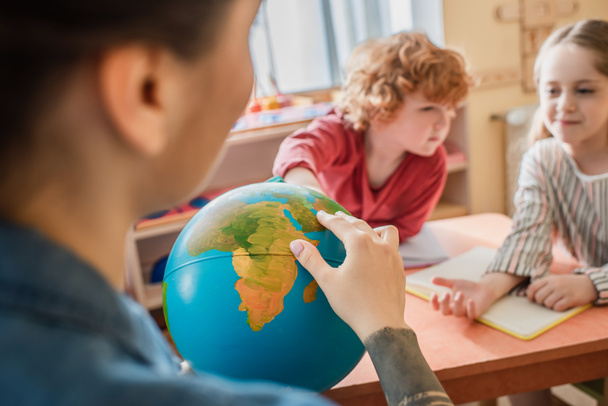 selectieve focus van globe in handen van leraar in de buurt van kinderen in Montessori school - Foto, afbeelding