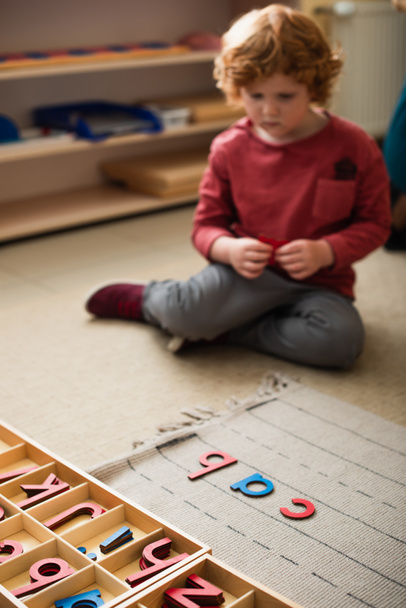 bambino sfocato seduto sul pavimento vicino a lettere di legno nella scuola montessori - Foto, immagini