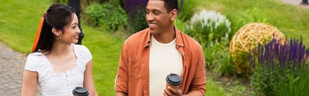 幸せな異人種間のカップルが公園を歩いてコーヒーを飲みに行き - 写真・画像