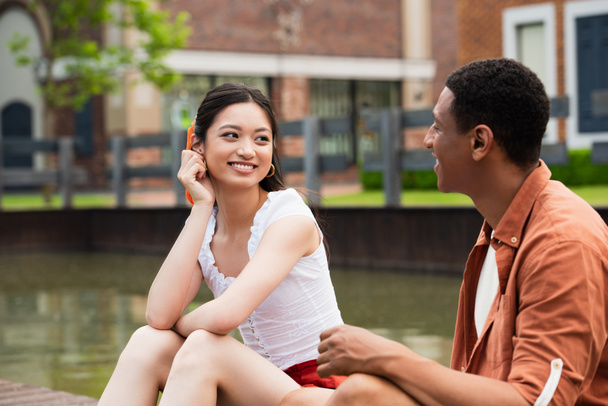 happy multicultural couple talking while sitting on urban street - Foto, Imagem