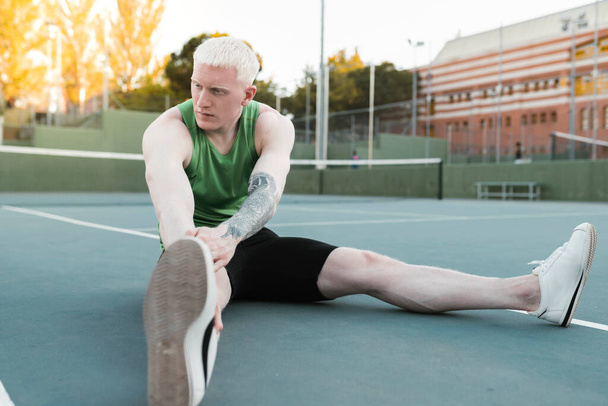 handsome male albino athlete stretching on a tennis court - Foto, afbeelding