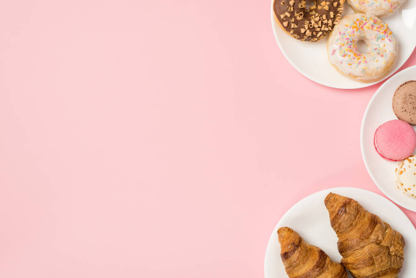 Верхняя фотография глазированных пончиков круассаны и различные макароны изолированы на розовом фоне с пустым местом - Фото, изображение