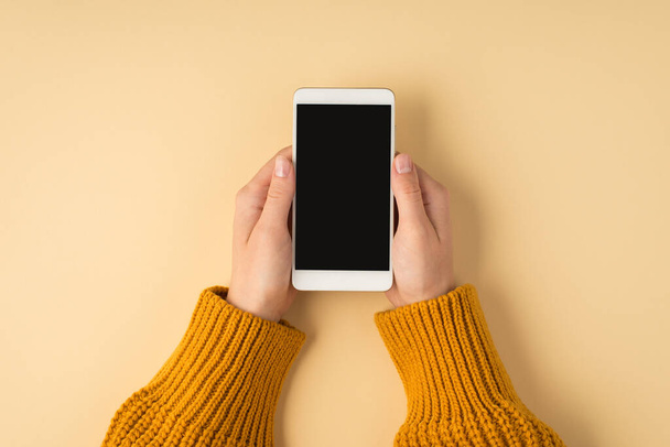 First person top view photo of female hands in yellow sweater holding white smartphone on isolated pastel orange background with copyspace - Valokuva, kuva