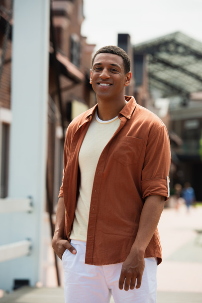 boldog afro-amerikai férfi áll kéz a kézben a zsebében a város utcáján - Fotó, kép