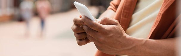 vista parcial del hombre afroamericano mensajería en el teléfono celular al aire libre, pancarta - Foto, Imagen