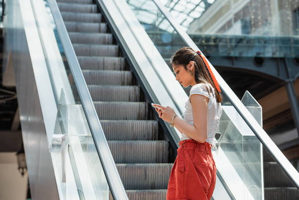 young asian woman messaging on mobile phone on escalator - Foto, Imagem
