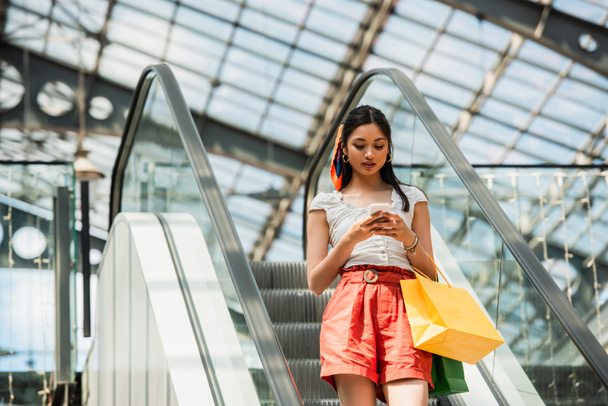 jolie asiatique femme avec shopping sacs messagerie sur téléphone portable sur escalator - Photo, image