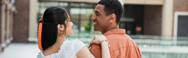 joven interracial pareja sonriendo el uno al otro al aire libre, bandera - Foto, imagen