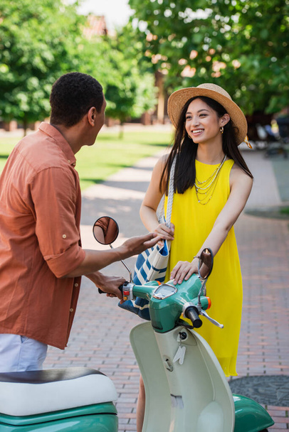 Africano americano homem falando com elegante asiático mulher perto de scooter ao ar livre - Foto, Imagem