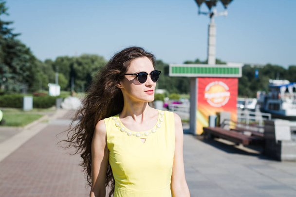 Beautiful girl in a yellow dress walks in a summer park on a sunny morning - Fotoğraf, Görsel