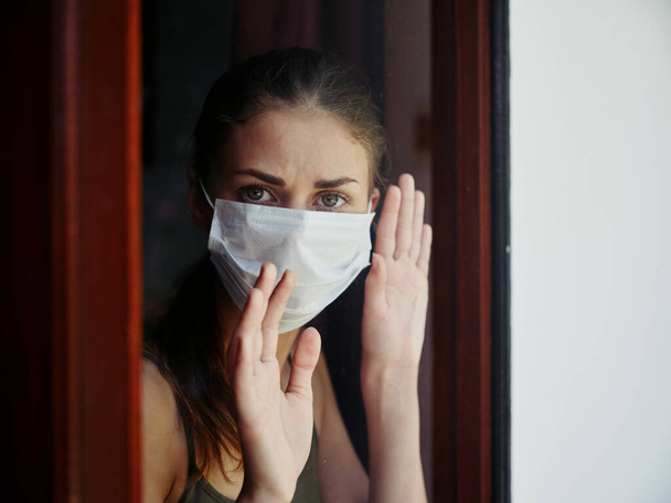 žena v lékařské masce při pohledu z okna smutný výraz uzamčení - Fotografie, Obrázek