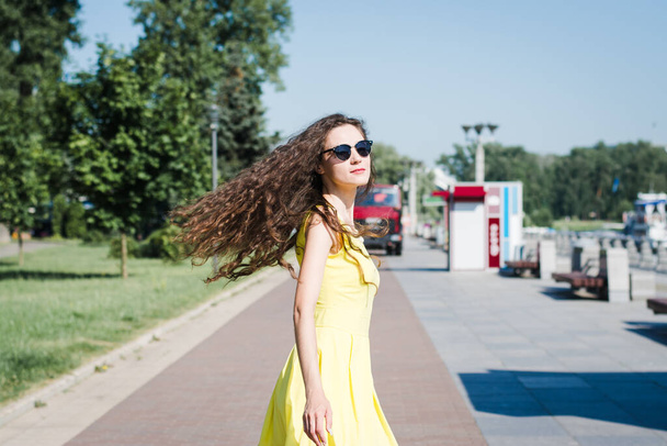 Beautiful girl in a yellow dress walks in a summer park on a sunny morning - Zdjęcie, obraz
