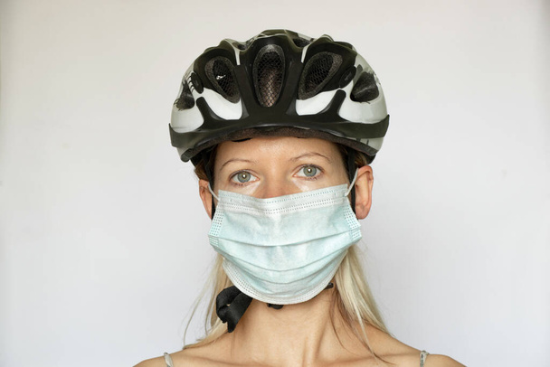 девушка в велосипедном шлеме и медицинской маске на белом фоне, во главе с портом в медицинской маске, пандемия - Фото, изображение