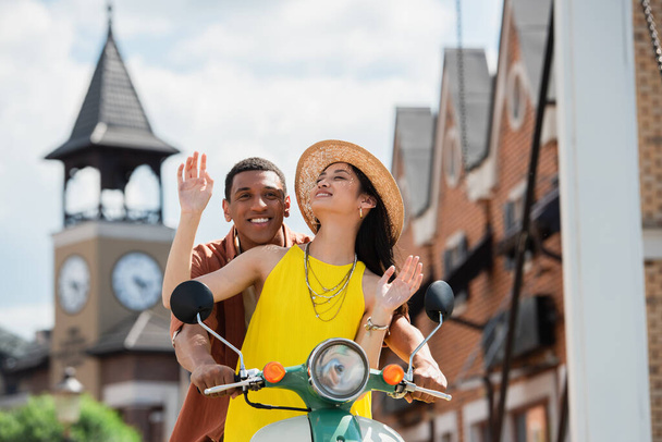 joyful asian woman in straw hat riding scooter with happy african american man - Photo, image