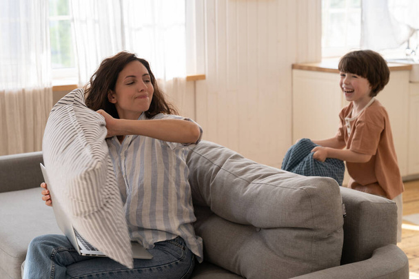 Mamma spensierata si diverte con il figlio in età prescolare in soggiorno giocando divertente lotta cuscino sul divano a casa - Foto, immagini