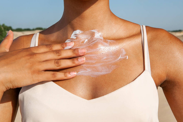 mulher de pele escura aplicando creme branco em seu peito enquanto estava na areia no verão - Foto, Imagem