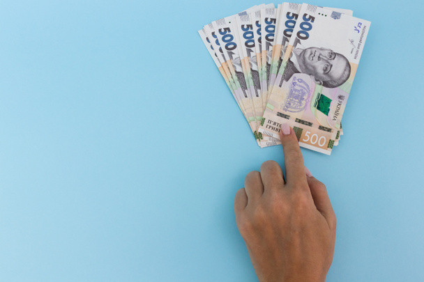 Der Finger zeigt auf Geld. Ukrainische Griwna. Auf blauem Hintergrund. - Foto, Bild