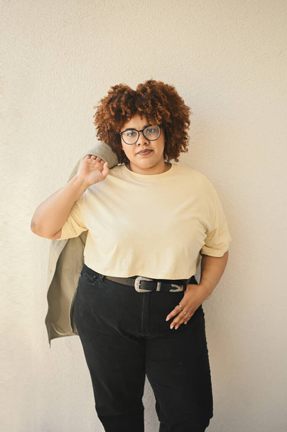 Beautiful happy smiling curvy plus size African black woman afro hair posing in beige t-shirt, jeans, stylish glasses on beige background. Body imperfection, acceptance body positive diversity concept - Photo, Image