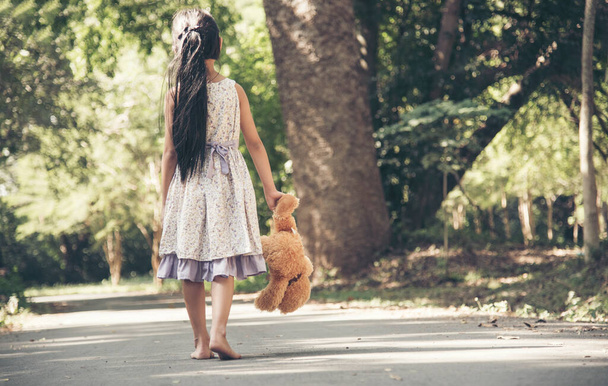 Sad girl hugging teddy bear sadness alone in green garden park. Lonely girl feeling sad unhappy walking outdoors with best friend toy. Autism child play teddy bear best friend. Family violence concept - Foto, Imagen