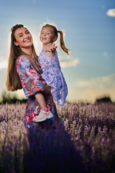 Happy mother and daughter having a great time in a lavender field at sunset - Φωτογραφία, εικόνα