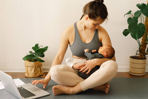 Мать держит новорожденного сына и работает за компьютером дома. - Фото, изображение