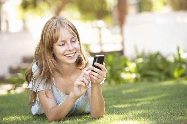 Teenage Girl Laying In Park Using Mobile Phone - Foto, afbeelding