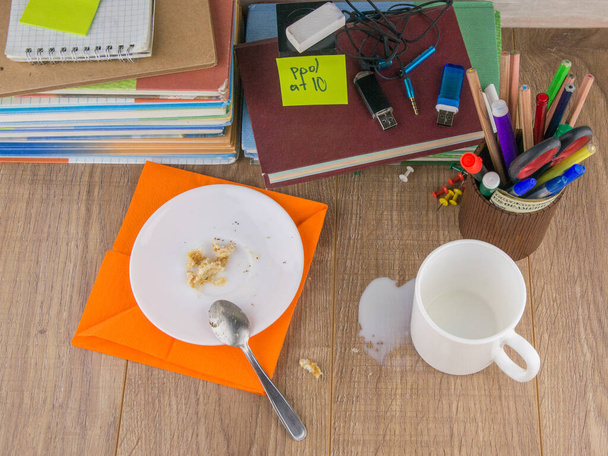 bagunça a estudante-sujeira: xícara, migalhas de bolo e uma colher de chá de laranja em um guardanapo em uma chapa, leite derramado e migalhas do bolo espalhadas na área de trabalho, vista superior - Foto, Imagem