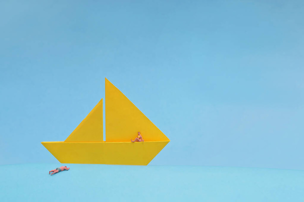 Barco de papel amarillo conceptual y personas en miniatura sobre fondo azul - Foto, Imagen