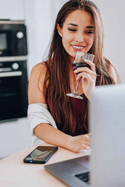attractive Asian woman drinking wine with friends online via a laptop. - Fotó, kép