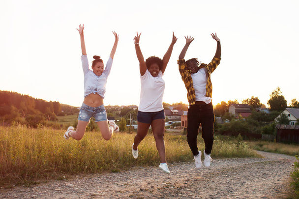 χαρούμενα κορίτσια διαφορετικών εθνικοτήτων πηδούν και διασκεδάζουν το ηλιοβασίλεμα το καλοκαίρι. - Φωτογραφία, εικόνα