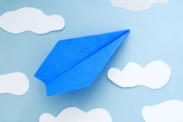 μπλε χάρτινο αεροπλάνο και σύννεφα, σε μπλε φόντο. - Φωτογραφία, εικόνα