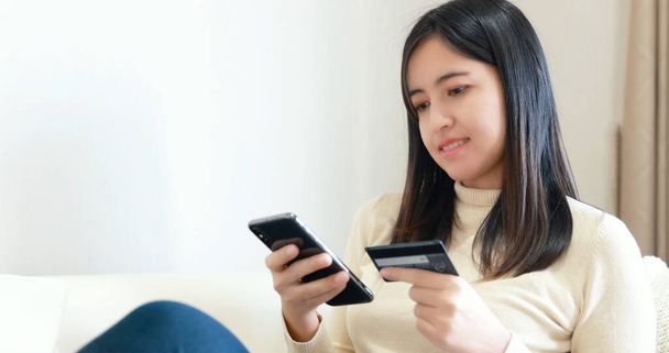 Kanepede oturan ve online alışveriş için akıllı telefon ve kredi kartı kullanan bir kadın. - Fotoğraf, Görsel