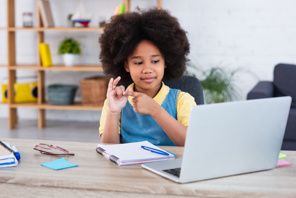 African american girl counting on fingers near laptop and stationery on table  - Фото, зображення