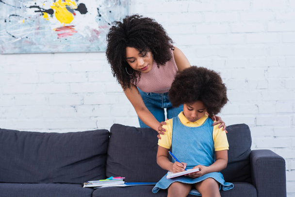 African american mother embracing kid writing on notebook at home  - Foto, Imagen