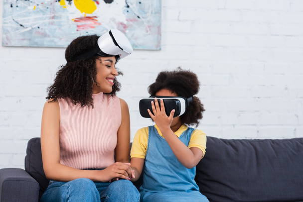 Uśmiechnięty afrykański rodzic patrzy na córkę w słuchawkach VR w domu  - Zdjęcie, obraz