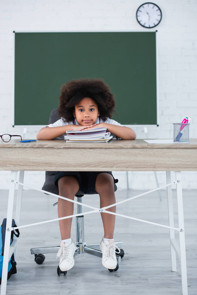 Африканська дівчинка - американка сидить біля книжки на столі в класі.  - Фото, зображення