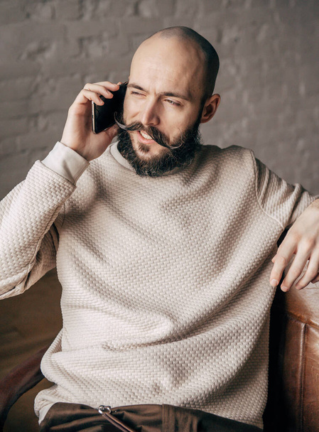 white young bald man with a beard is talking on the phone in the room - Foto, afbeelding