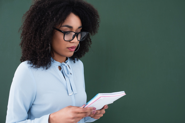 Professeur afro-américain en lunettes tenant un carnet près du tableau  - Photo, image