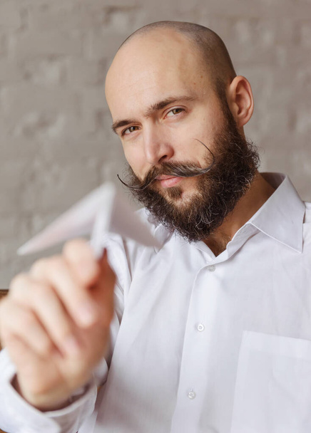 homme chauve avec une barbe dans une chemise blanche, avion en papier - Photo, image