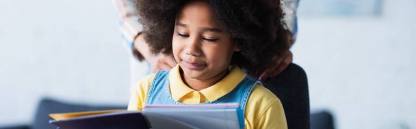 African american kid looking at notebook near blurred mother, banner  - Photo, Image
