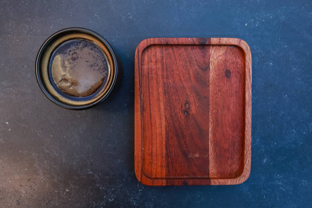 Black coffee cup and blank wooden pad. Dark mug of espresso or Americano on concrete table background. For coffee shop templates, cafe, breakfast concept. Top view - 写真・画像