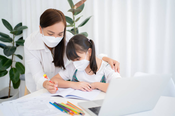 Mother and daughter studying online with Zoom program at home together. They wear masks while sitting in class together to prevent infection from the virus. Concept of health care and social distance - Foto, imagen