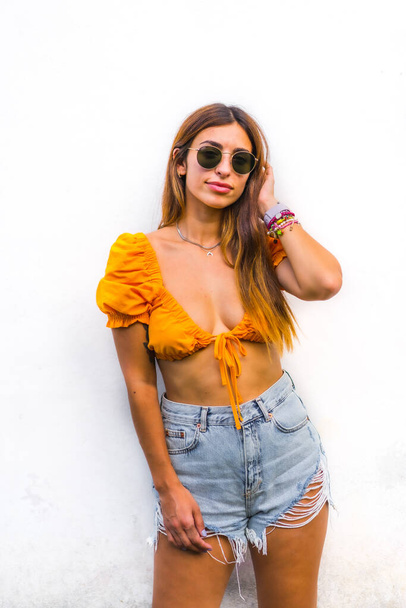 Lifestyle of a young caucasian brunette with orange t-shirt, sunglasses and short pants on a white background - Foto, immagini